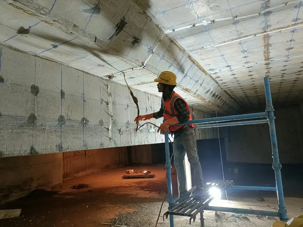 Worker performing PU injection grouting on a concrete ceiling with marked injection grid points, using a hand-held injection hose.