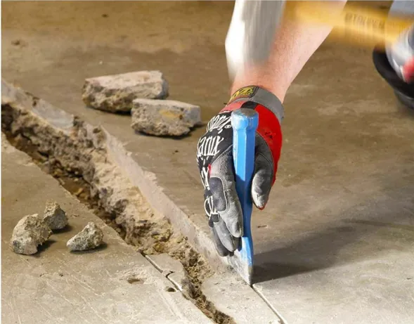 Worker removing loose debris and chiseling concrete crack channel
