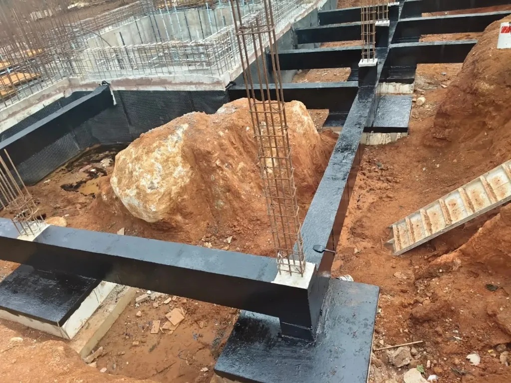 Waterproof coated foundation beams around an excavated boulder on site