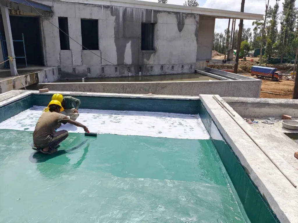 Worker applying green pigmented waterproof topcoat to a terrace and parapet wall